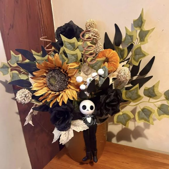 Pot arrangement of a sunflower, black roses and ivy, with a skeleton figure