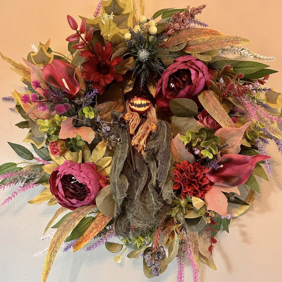 Halloween wreath of red and pink peonies, sunflowers and autumn leaves, with a small witch figure in the centre