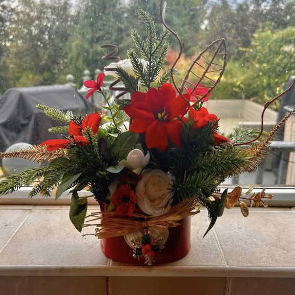 Red poinsettias, pine and white roses arranged in a red tin on a windowsill