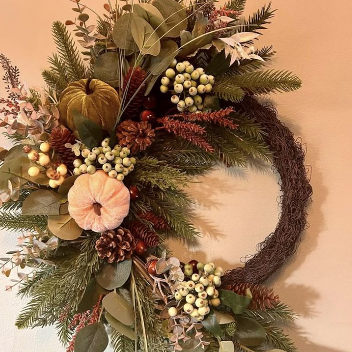 Grapevine wreath dressed on one side with pine, eucalyptus, berries, pine cones and pumpkins