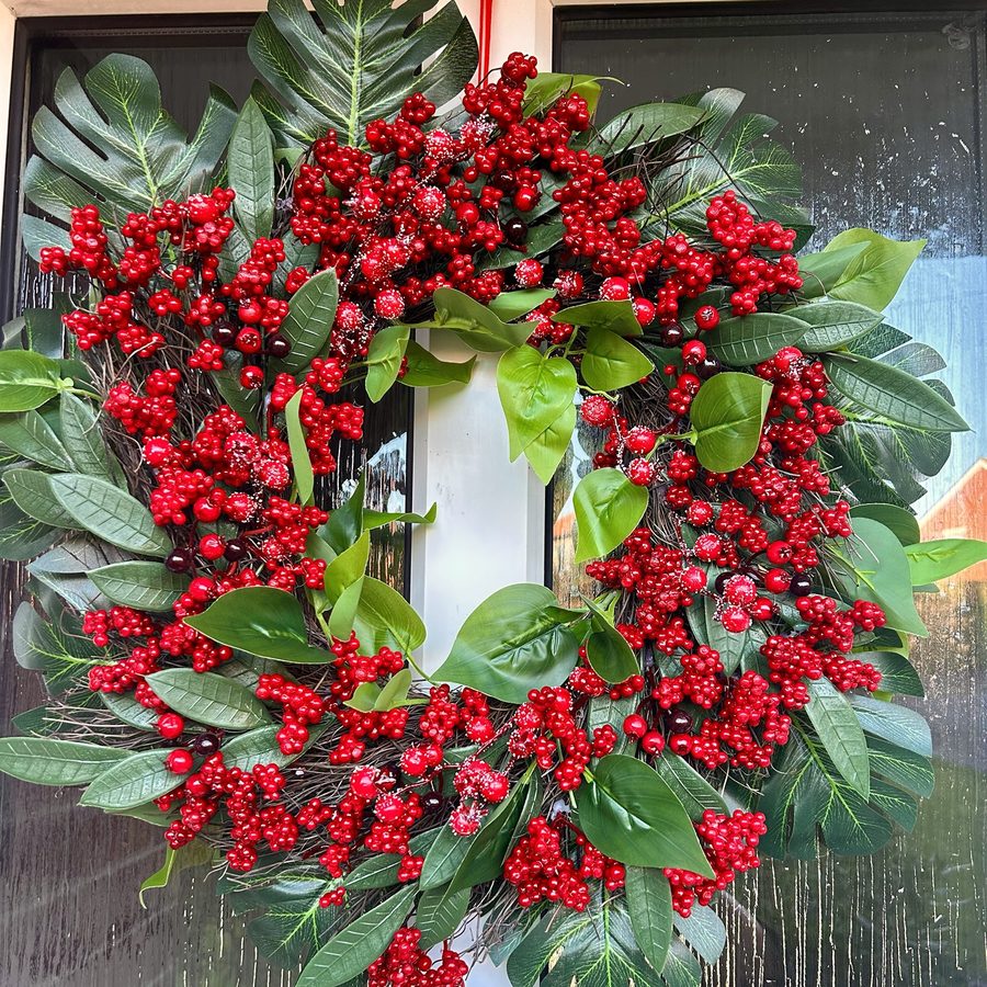 Wreath of red and frosted berries with large green leaves on a twig base, hanging on a front door