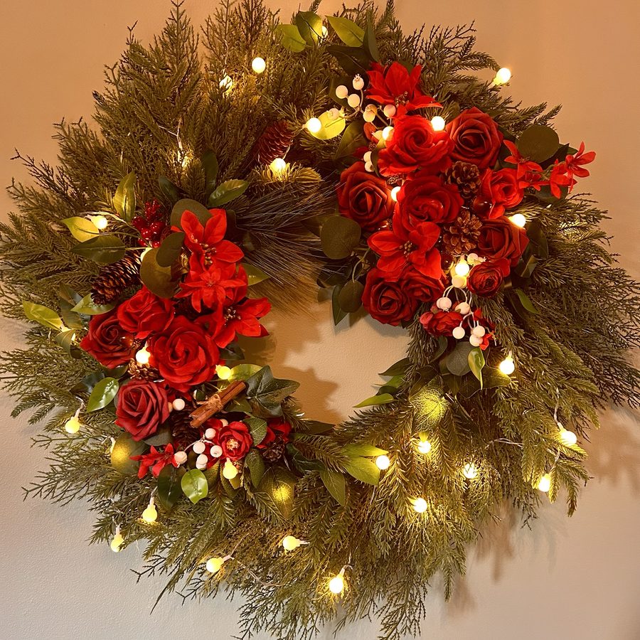 Pine wreath with red roses, poinsettias, pine cones, cinnamon sticks and white berries, lit with warm fairy lights