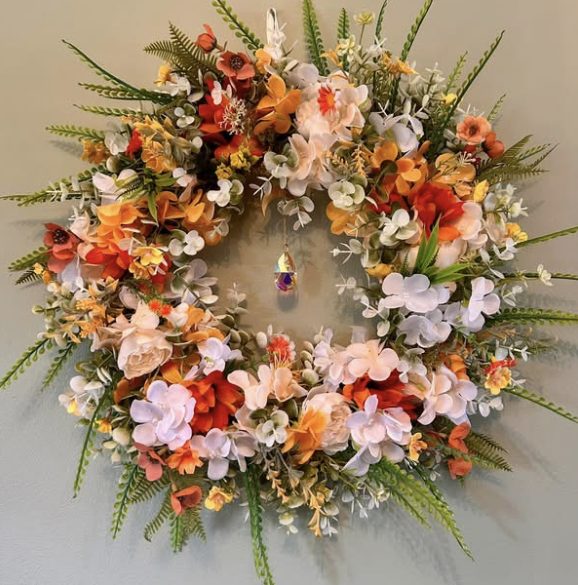 Spring wreath of peach, orange and white flowers with a crystal hanging in the centre