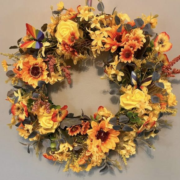 Round wreath of yellow roses, sunflowers and orange flowers, with a rainbow butterfly